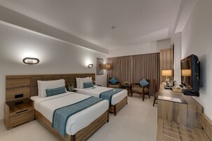 Een hotelkamer met twee bedden, een bureau, een stoel, een televisie en een spiegel.