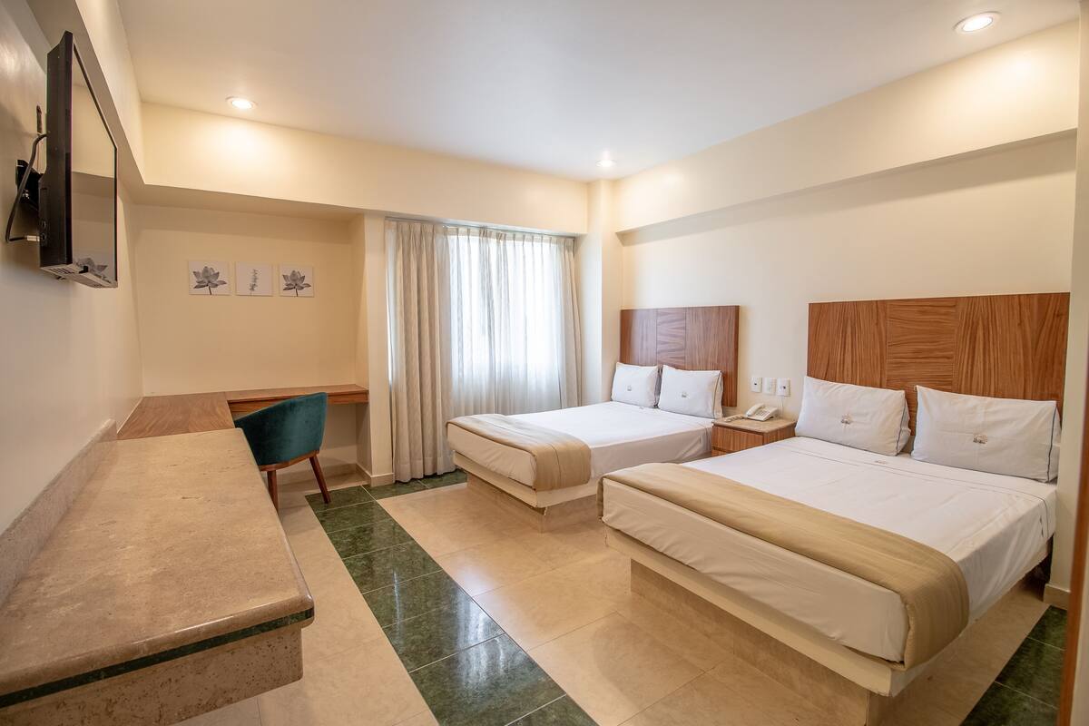 A hotel room with two beds, a desk, a chair, and a TV mounted on the wall.