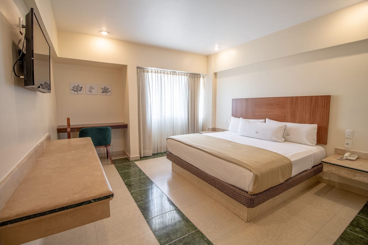 A hotel room with a bed, bedside table, desk, chair, and a television mounted on the wall.