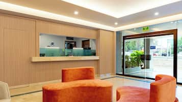 A modern reception area with a glass door entrance, a reception desk, and a seating area with orange upholstered chairs.