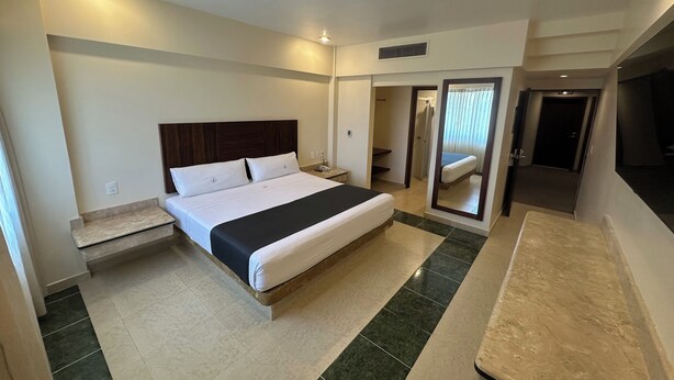 Habitación de hotel con una cama grande, una mesita de noche, un espejo y un baño visible a través de una puerta abierta.