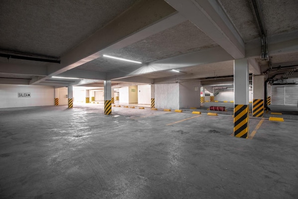 Un estacionamiento vacío con pisos de concreto, pilares con franjas amarillas y negras, y un letrero que dice 'SALIDA'.