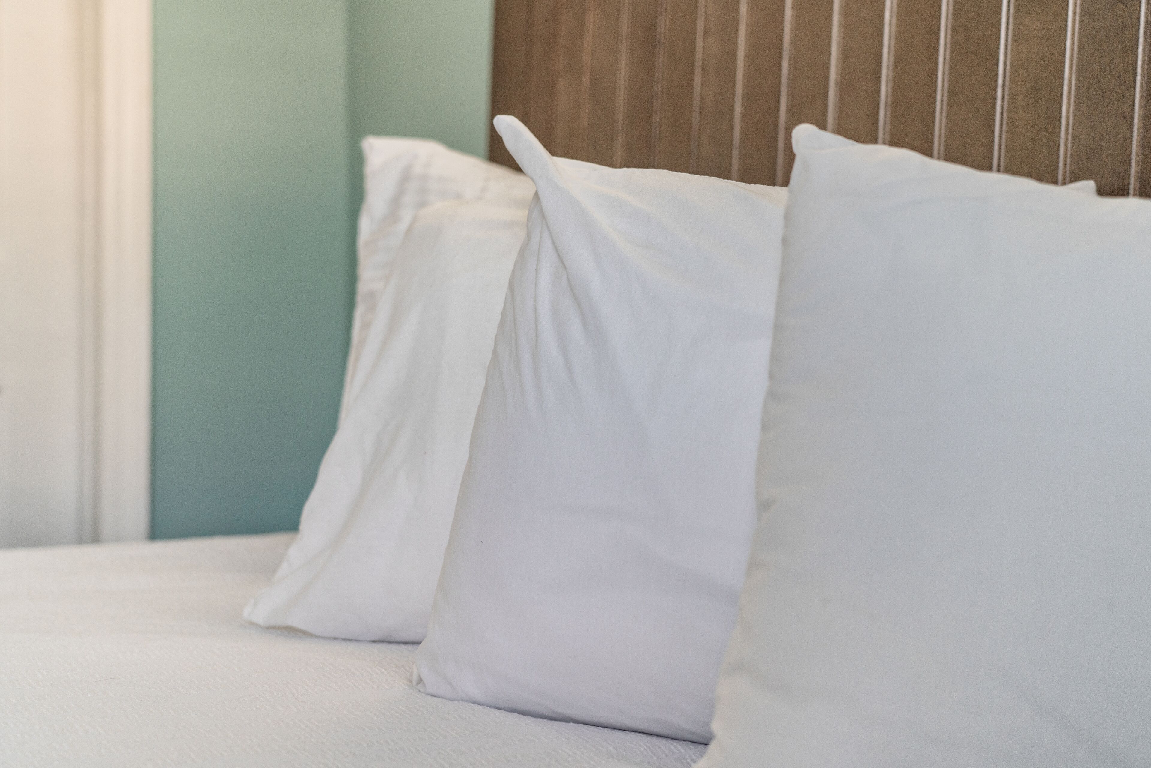 A bed with white bedding and pillows, a wooden headboard, and a teal wall.