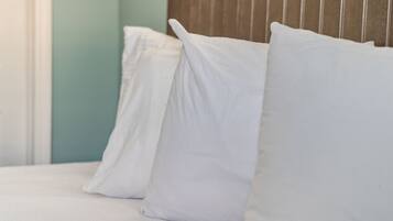 A bed with white bedding and pillows, a wooden headboard, and a teal wall.
