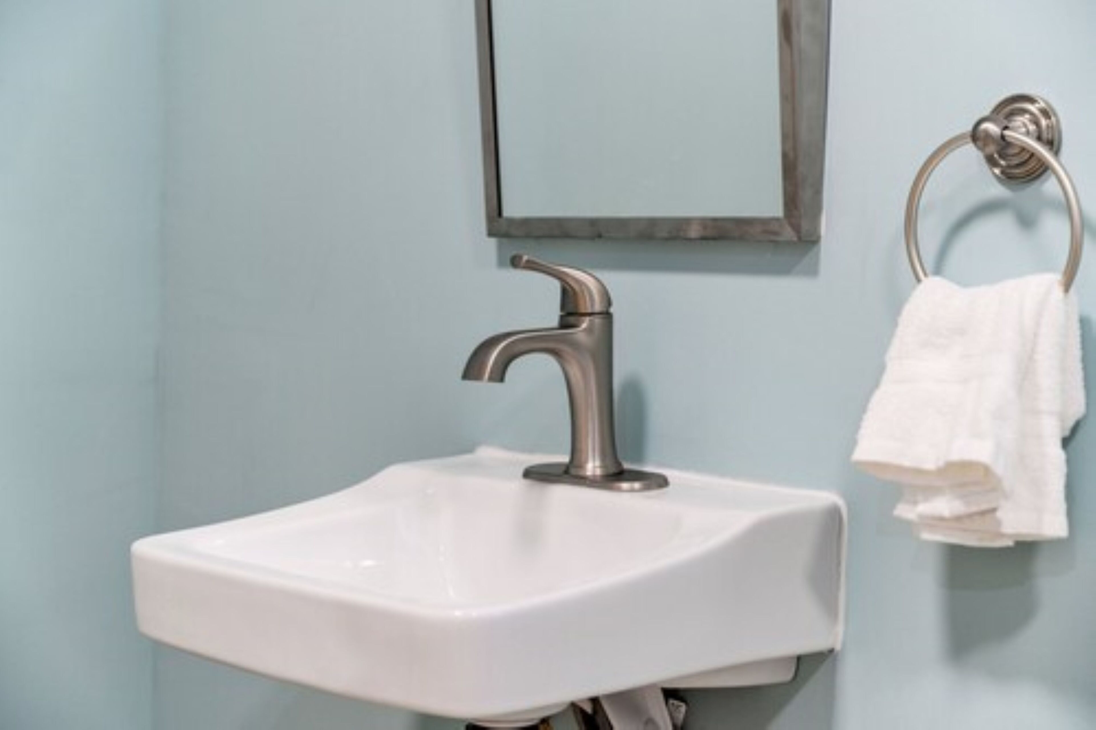 A bathroom with a white sink, a silver faucet, and a towel rack with a white towel.