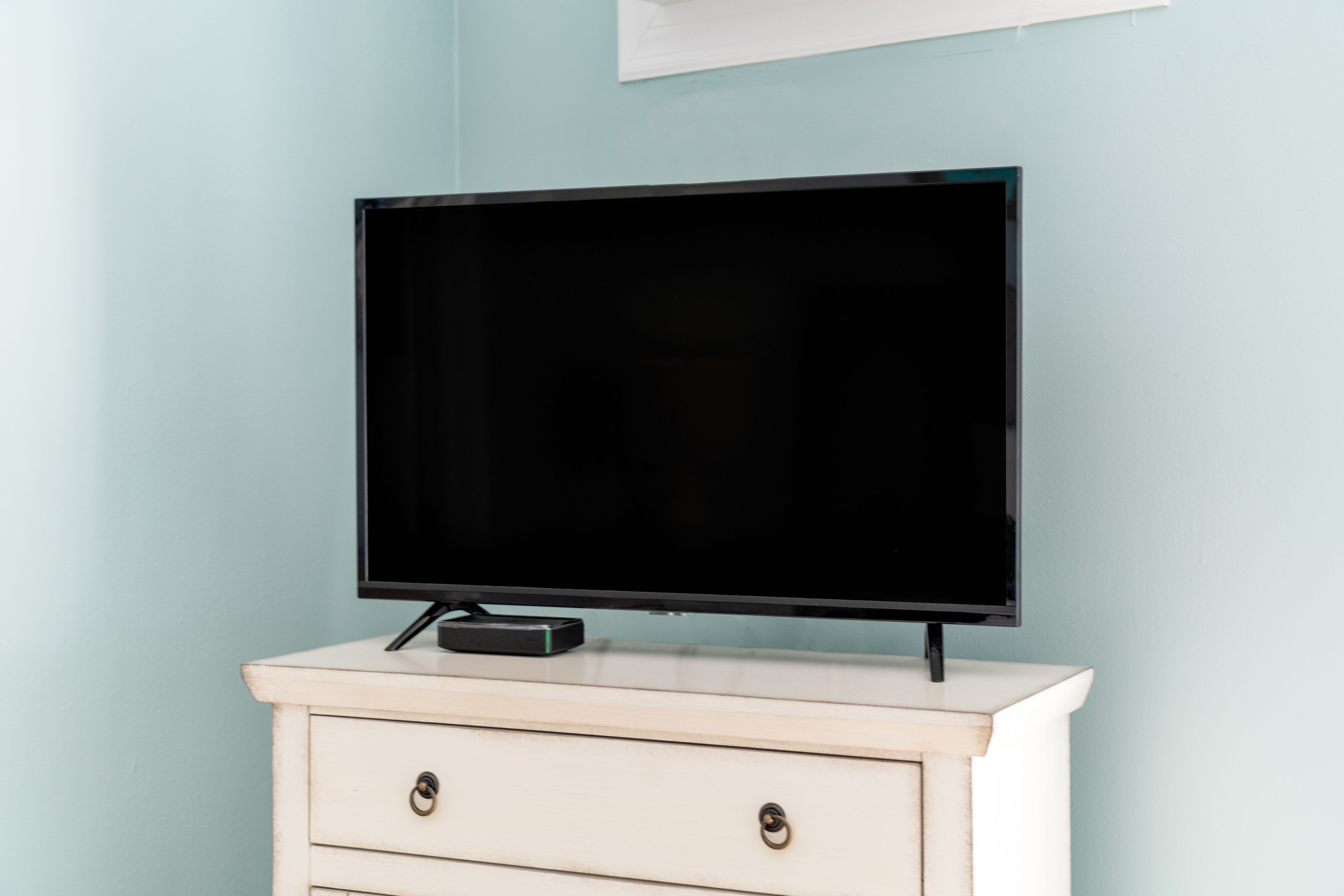 A television on a white dresser against a light blue wall.