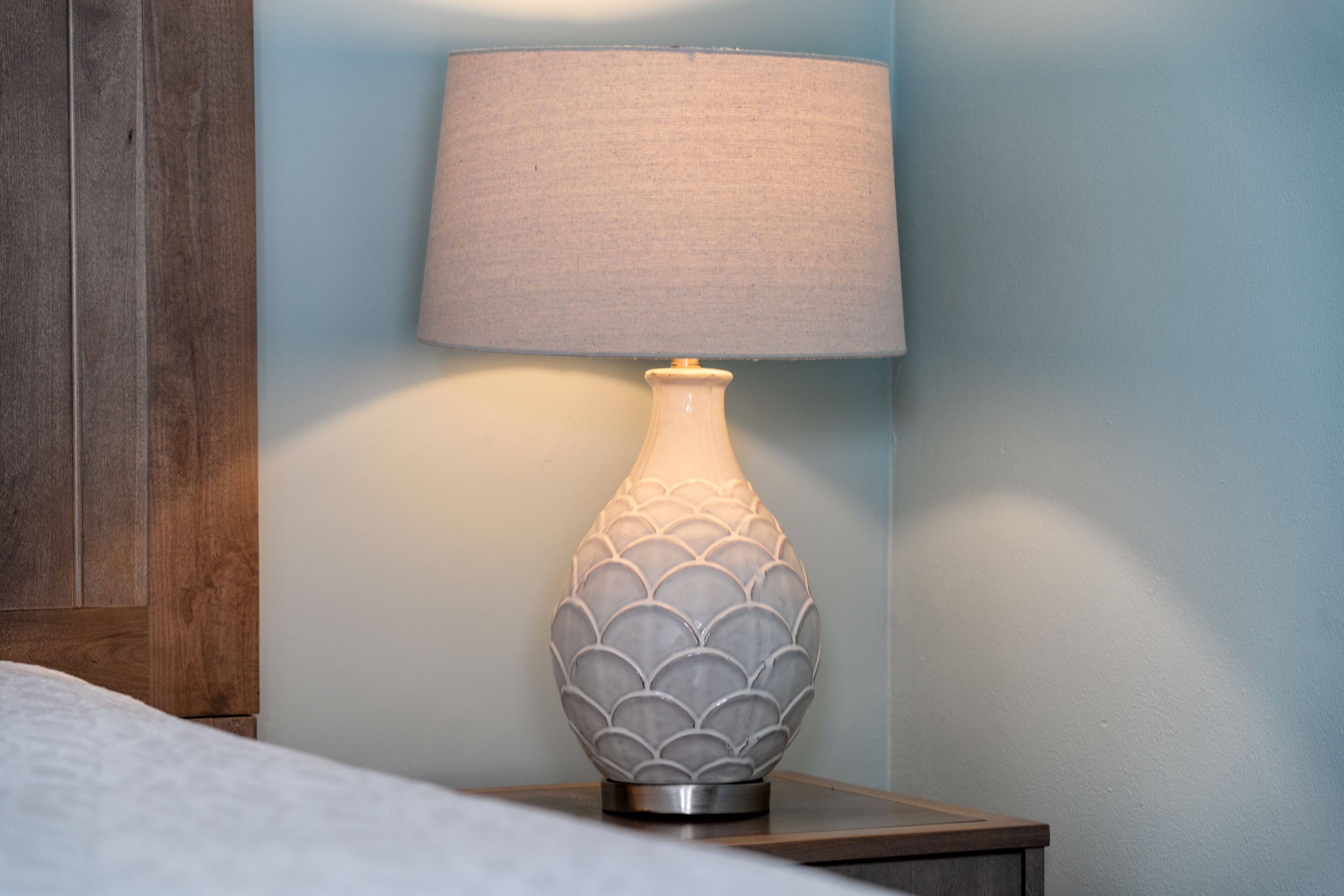A lamp with a textured, scalloped design on a bedside table against a blue wall.