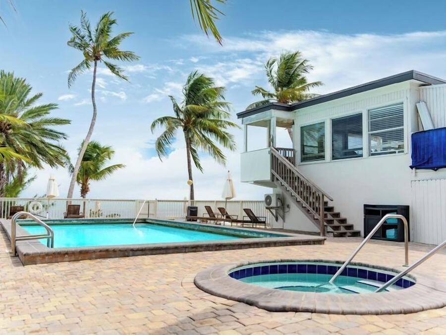 A swimming pool with a hot tub, palm trees, and a building with a staircase.