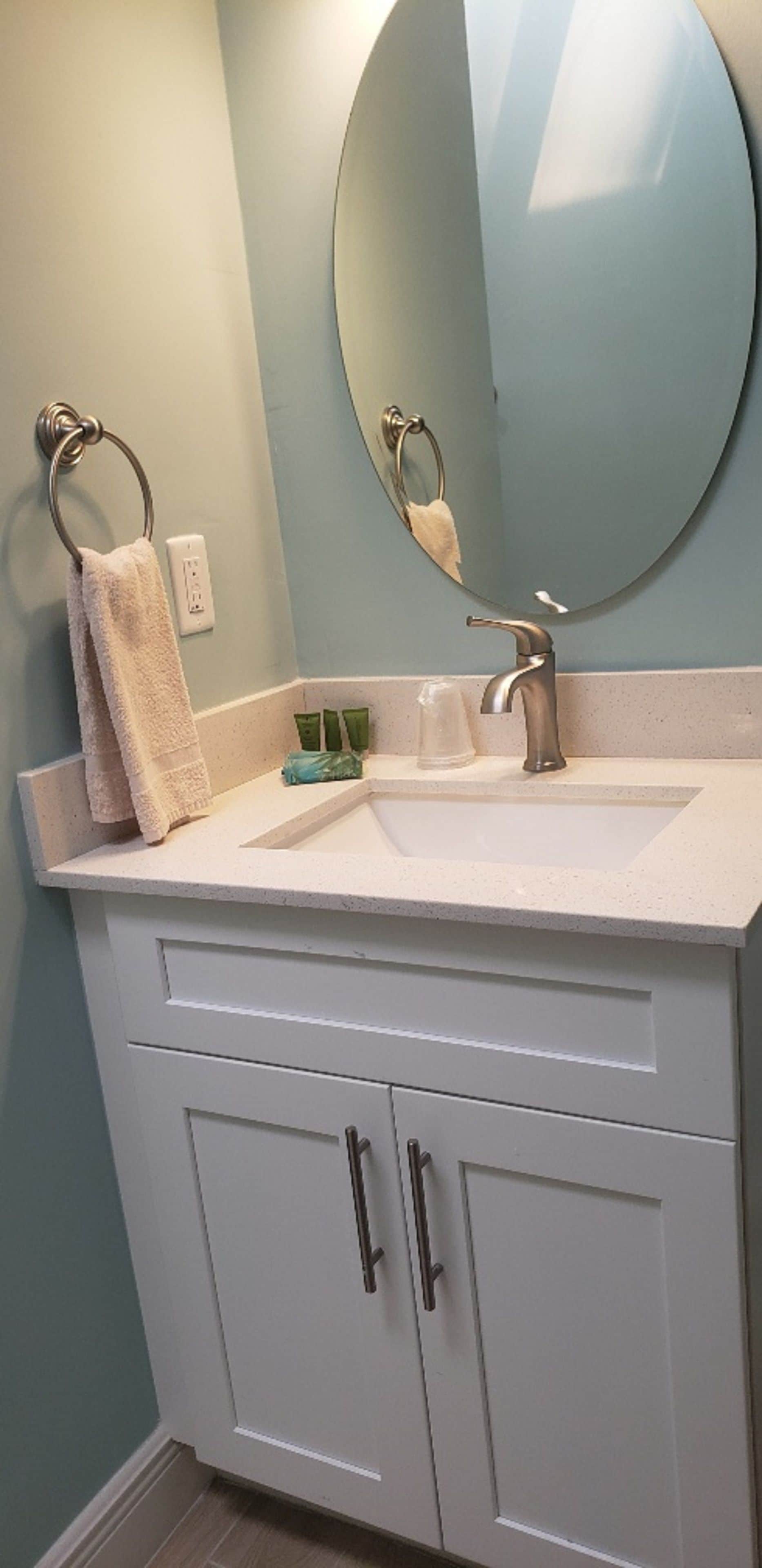 Une salle de bain avec un meuble-lavabo blanc, un miroir rond, un porte-serviettes et un lavabo avec un robinet.
