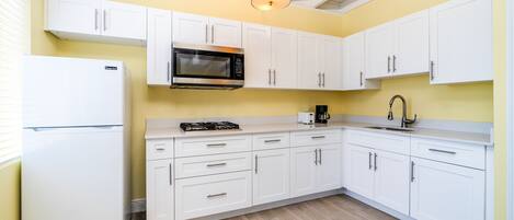 A modern kitchen with white cabinets, a stainless steel microwave, a gas stove, and a sink.