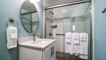 Un baño con lavamanos, espejo y cabina de ducha de vidrio.