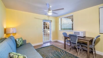 Un salon comprenant un canapé, une table à manger avec des chaises, un ventilateur de plafond et une fenêtre avec des stores.