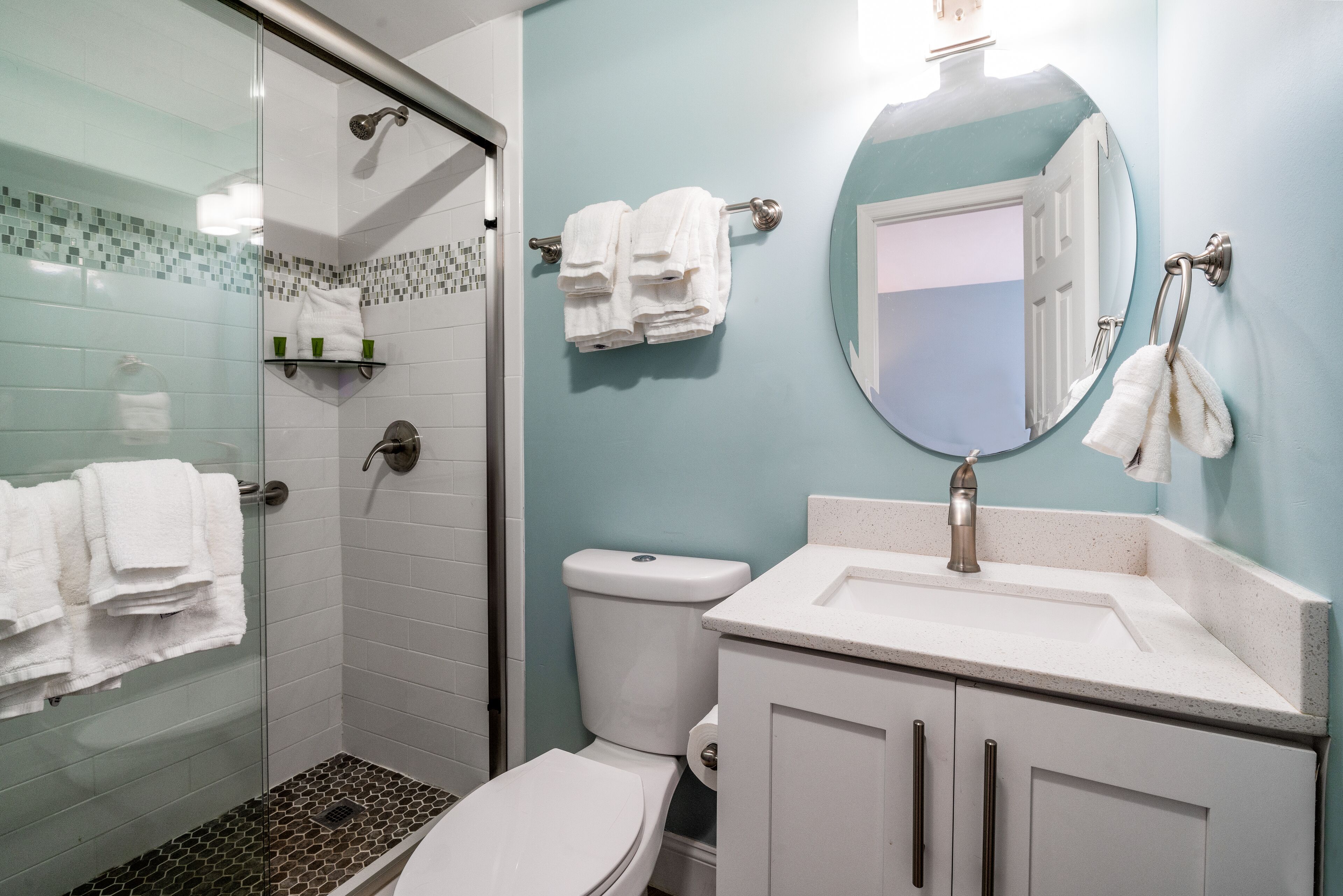 A bathroom with a glass shower enclosure, a toilet, a sink with a mirror, and towels on a rack.