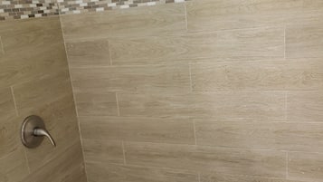 Un angolo doccia con pareti piastrellate e una fascia decorativa in mosaico.