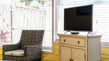 A room with a wicker chair, a television on a cabinet, and a window with blinds.
