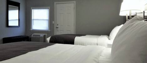 A hotel room with two beds, a window, a door, and a wall-mounted lamp.