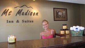 A reception desk at Mt. Madison Inn & Suites with a sign above indicating the name and slogan. There are candles and toiletries on the counter. - Mt Madison Inn & Suites (Gorham)