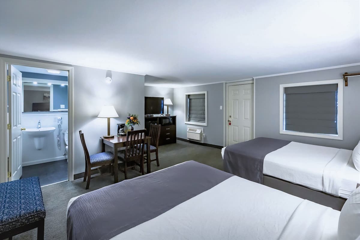 Ein Hotelzimmer mit zwei Betten, einem Schreibtisch mit Stuhl, einem Fernseher und einem durchgegangenen Tür erkennbaren Badezimmer.