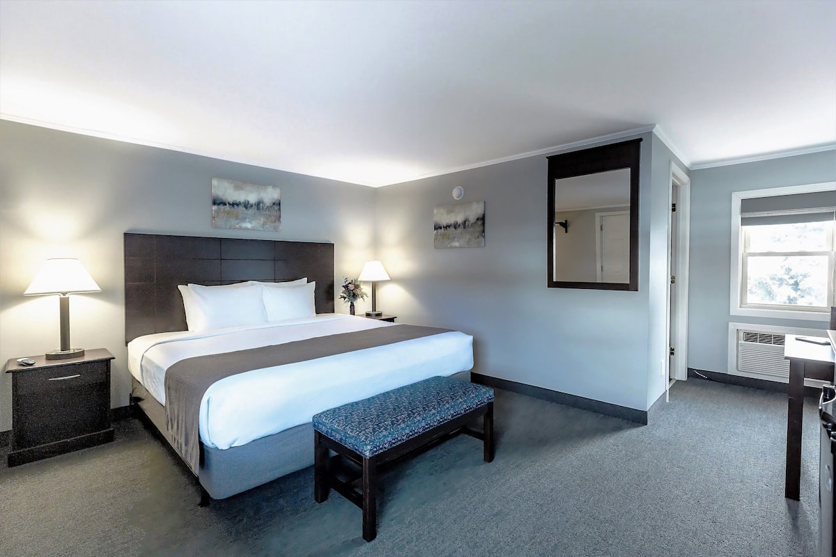 Ein Hotelzimmer mit einem großen Bett, zwei Nachttischen mit Lampen, einer Bank und Bildern an den Wänden.