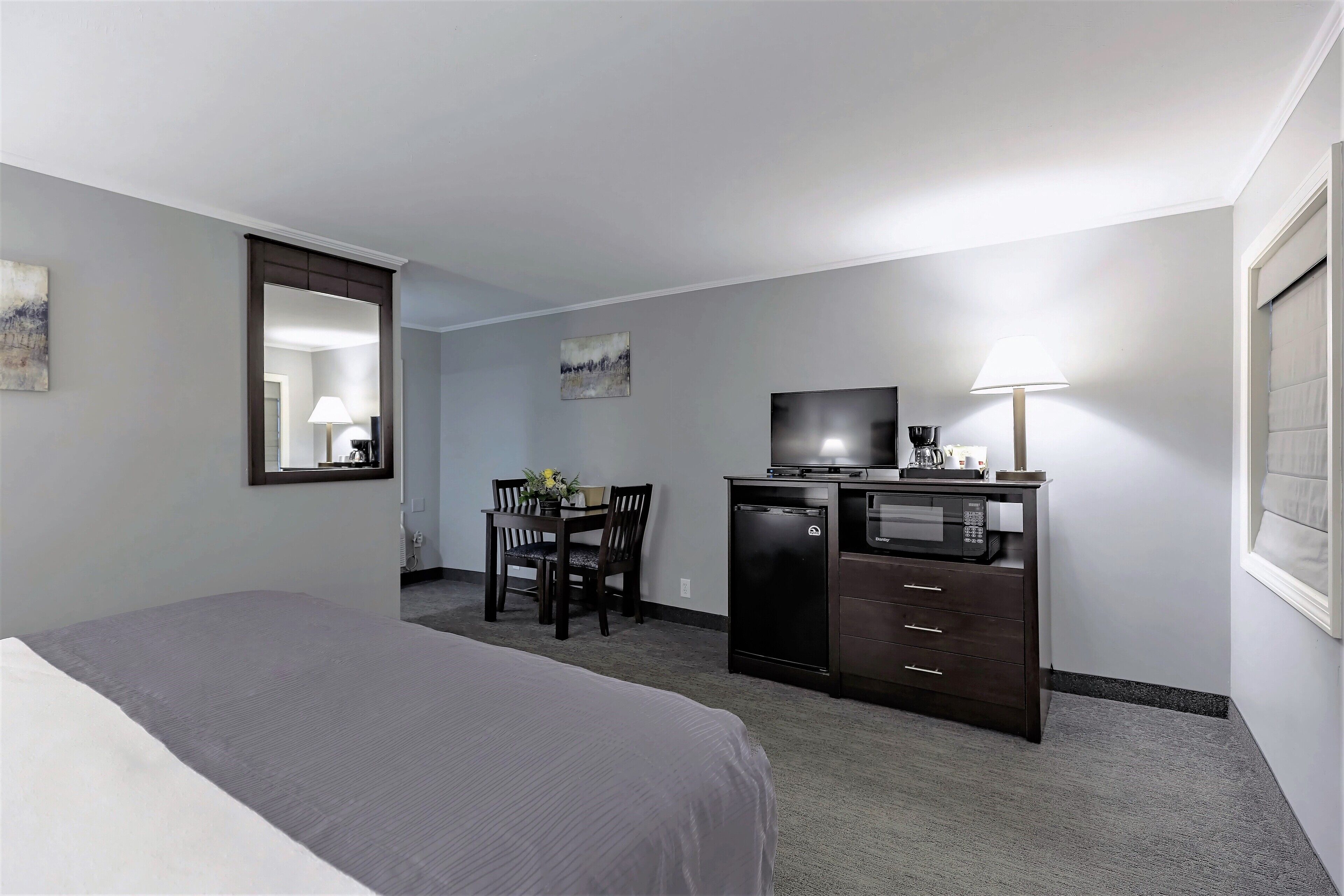 Une chambre d’hôtel équipée d’un lit, d’un bureau avec une chaise, d’une télévision, d’un four à micro-ondes et d’une lampe.