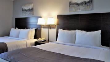 A hotel room with two beds, a nightstand with a lamp, and artwork on the walls.