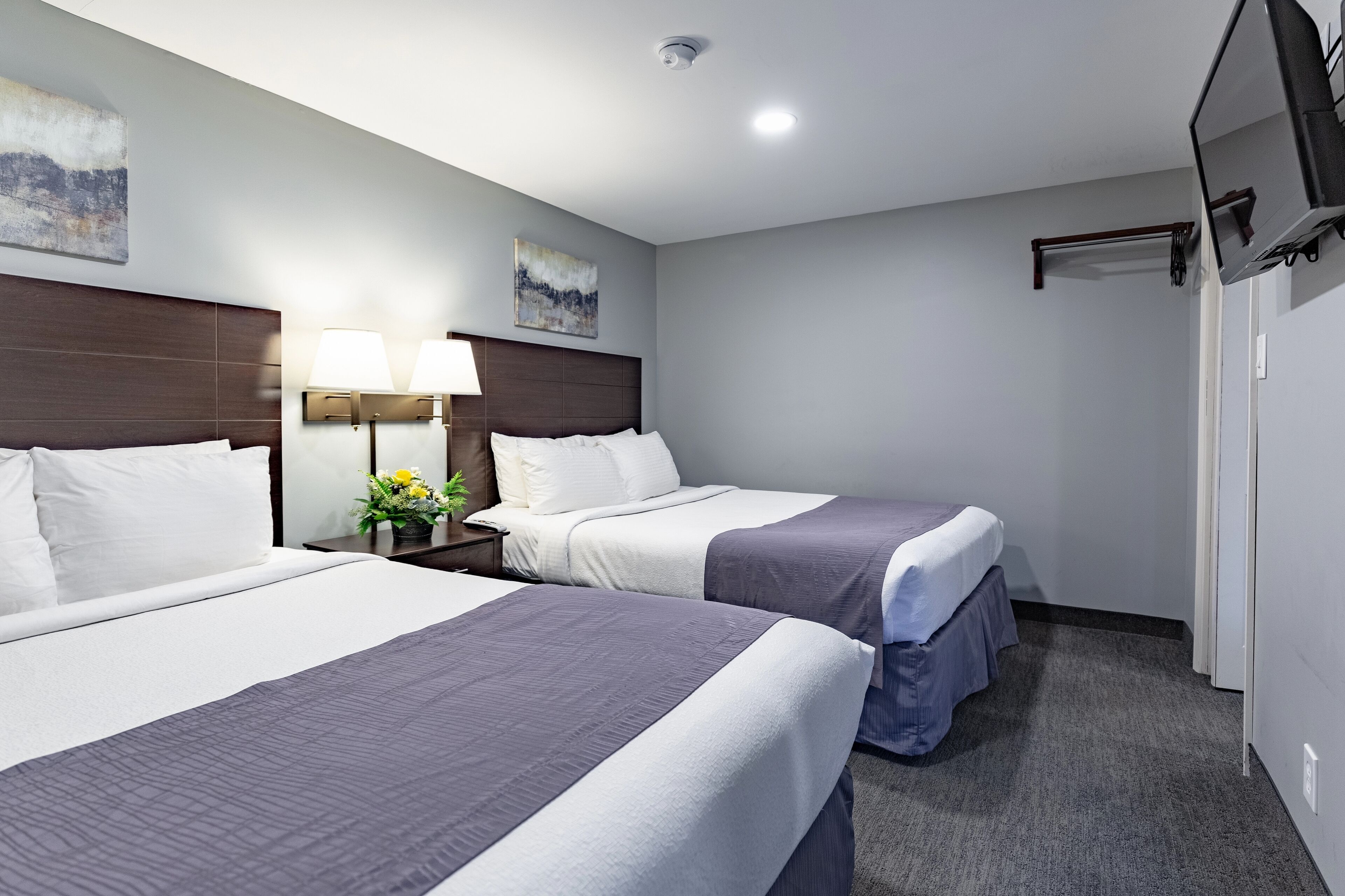 A hotel room with two beds, a nightstand with a lamp, and a painting on the wall.