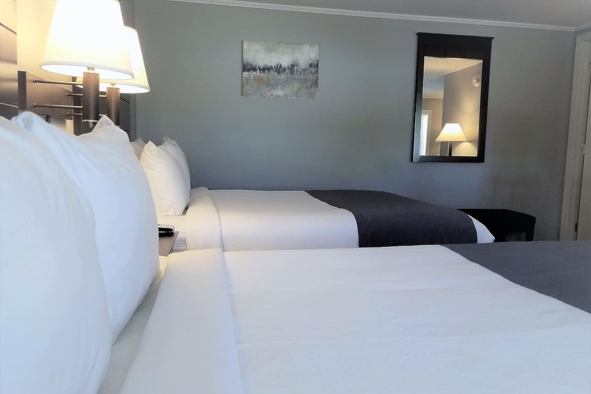 Ein Hotelzimmer mit zwei Betten, einem Nachttisch, einer Lampe, einem Bild und einem Spiegel.