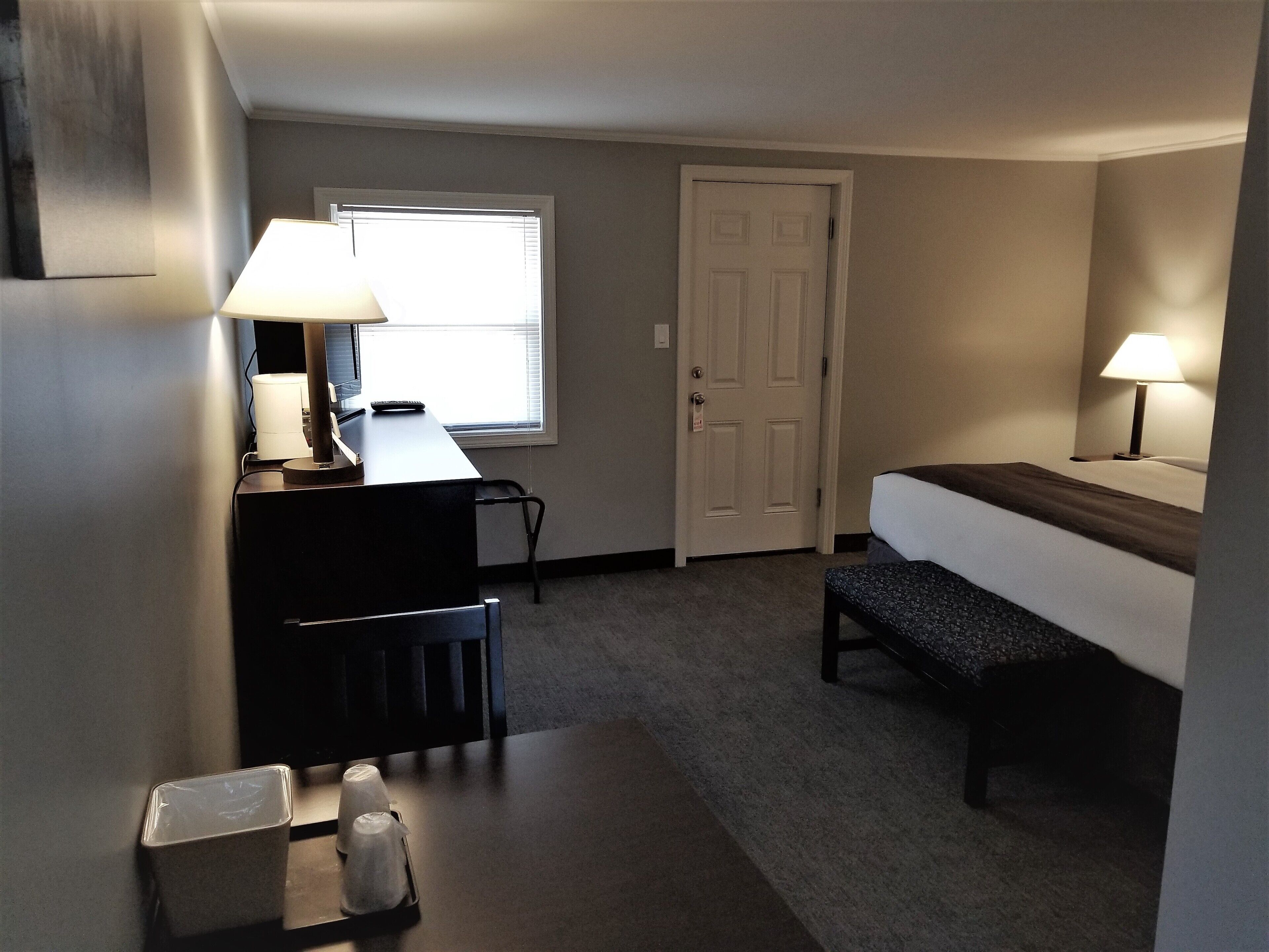 A small, well-lit room with a desk, chair, and a bed.