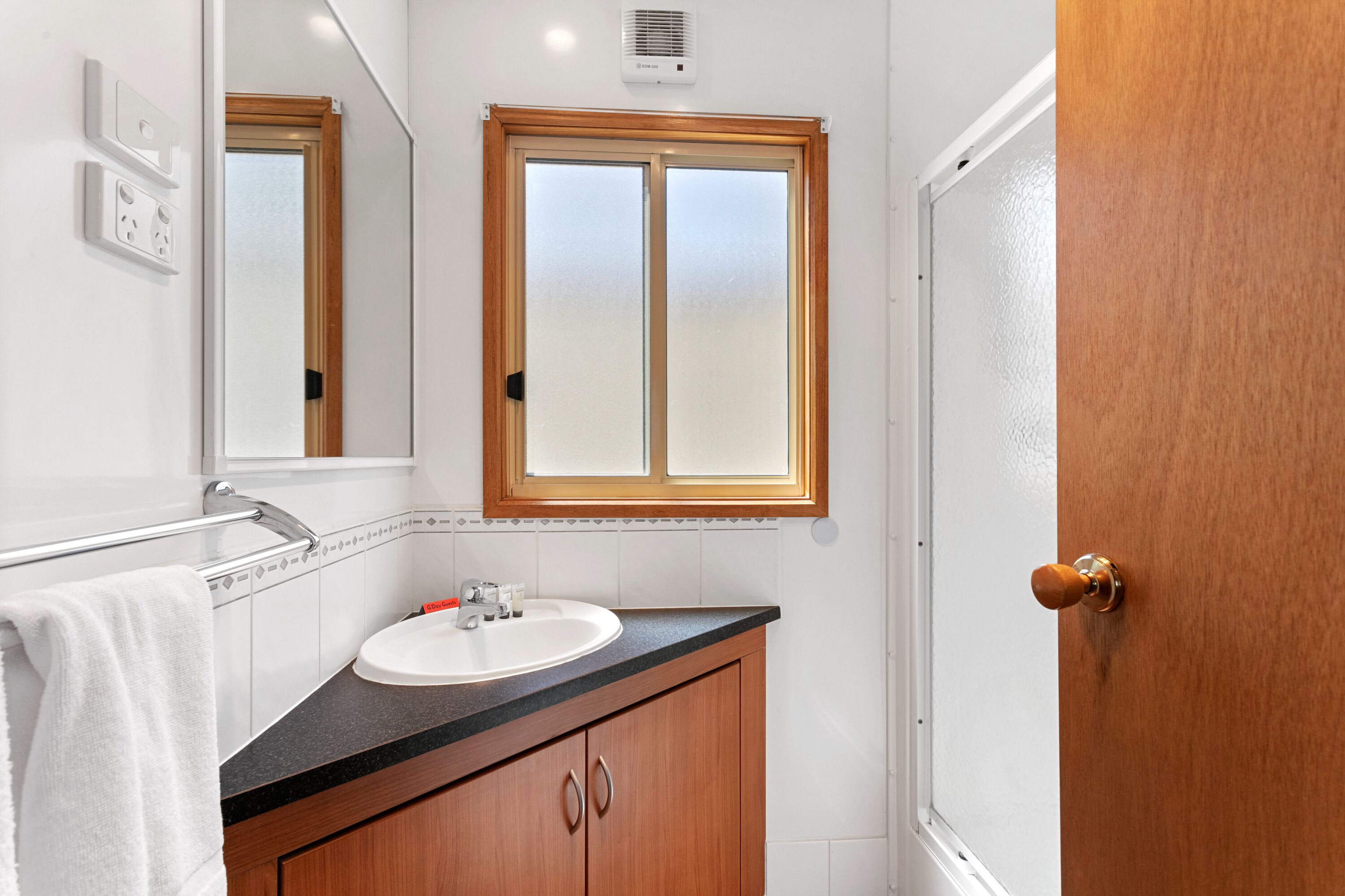 A bathroom with a wooden vanity, white sink, and a mirror above it.