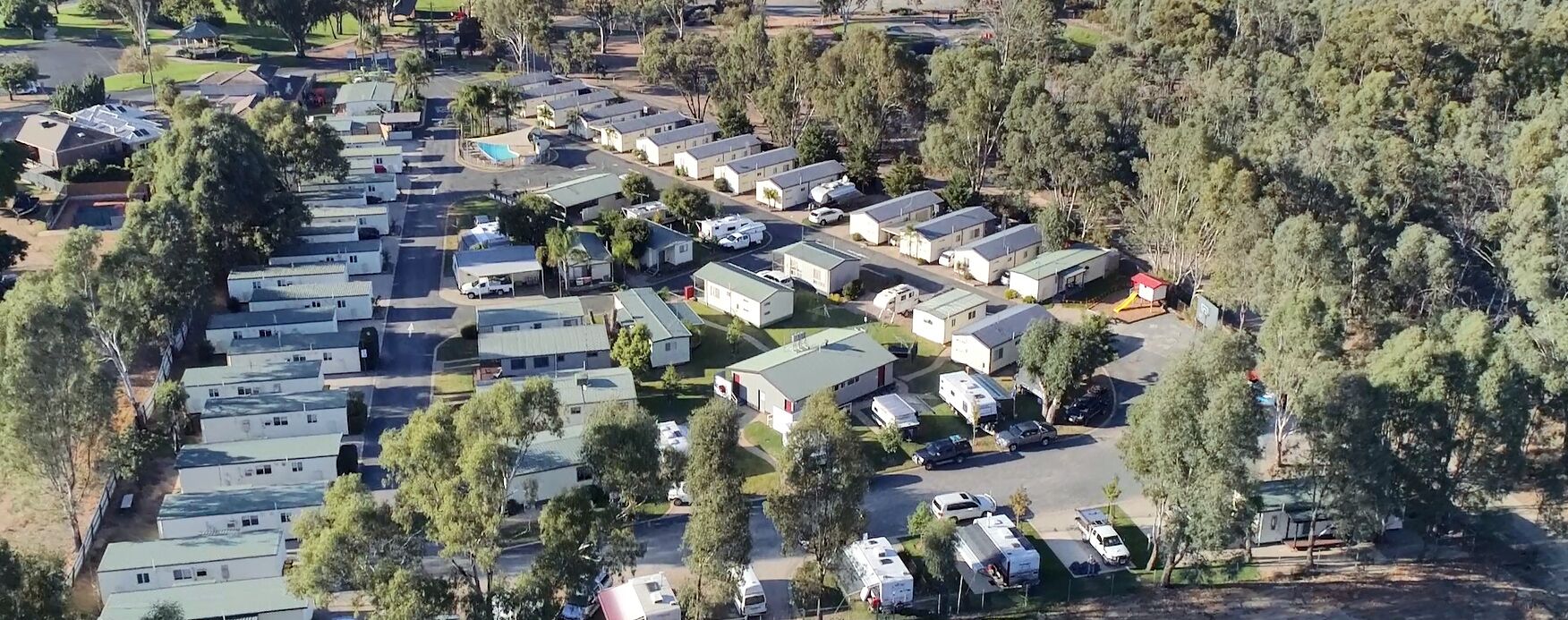 An aerial view of a caravan park with multiple caravan sites, surrounded by trees and greenery.
