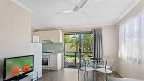 A modern kitchen with white cabinets, a microwave, and a stove. There is a dining area with a glass table and chairs, and a TV on a glass stand. - BIG4 Moama Holiday Park (Moama)