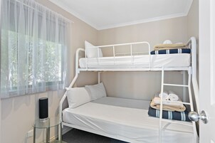 A bunk bed with a glass table beside it, a window with sheer curtains, and a door with a silver handle.