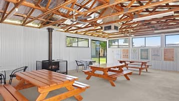 An outdoor covered area with picnic tables and chairs, a fireplace, and a view of the surrounding landscape.
