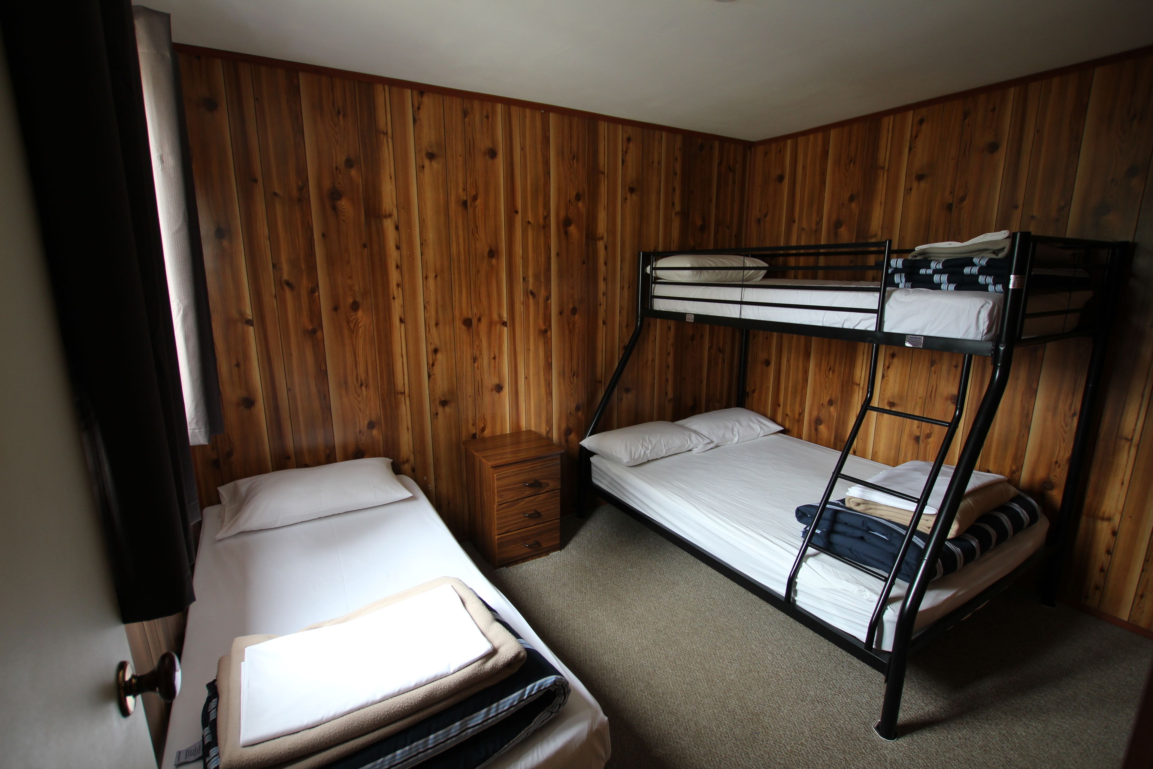 Une pièce avec deux lits superposés, un mur en bois, une petite table de chevet en bois et une porte avec un rideau.