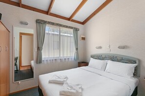 A hotel room with a large bed, a wardrobe, a mirror, a window with curtains, and a headboard with a patterned design.