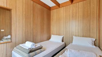 A room with two beds, wooden walls, a mirror, and neatly folded towels.