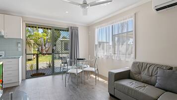 A modern living room with a grey sofa, a dining table with chairs, a ceiling fan, and a sliding glass door leading to a balcony.