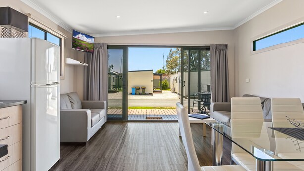 A modern living room with a glass dining table, a sofa, and a kitchen area with a refrigerator. - BIG4 Moama Holiday Park (Moama)