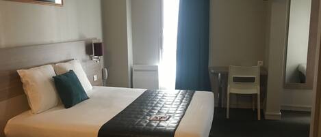 A hotel room with a bed, a desk, a chair, a TV, and a window with curtains.