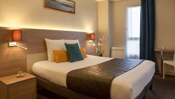 Une chambre d’hôtel avec un grand lit, des lampes de chevet, une petite table avec une tasse et une fenêtre avec des rideaux.