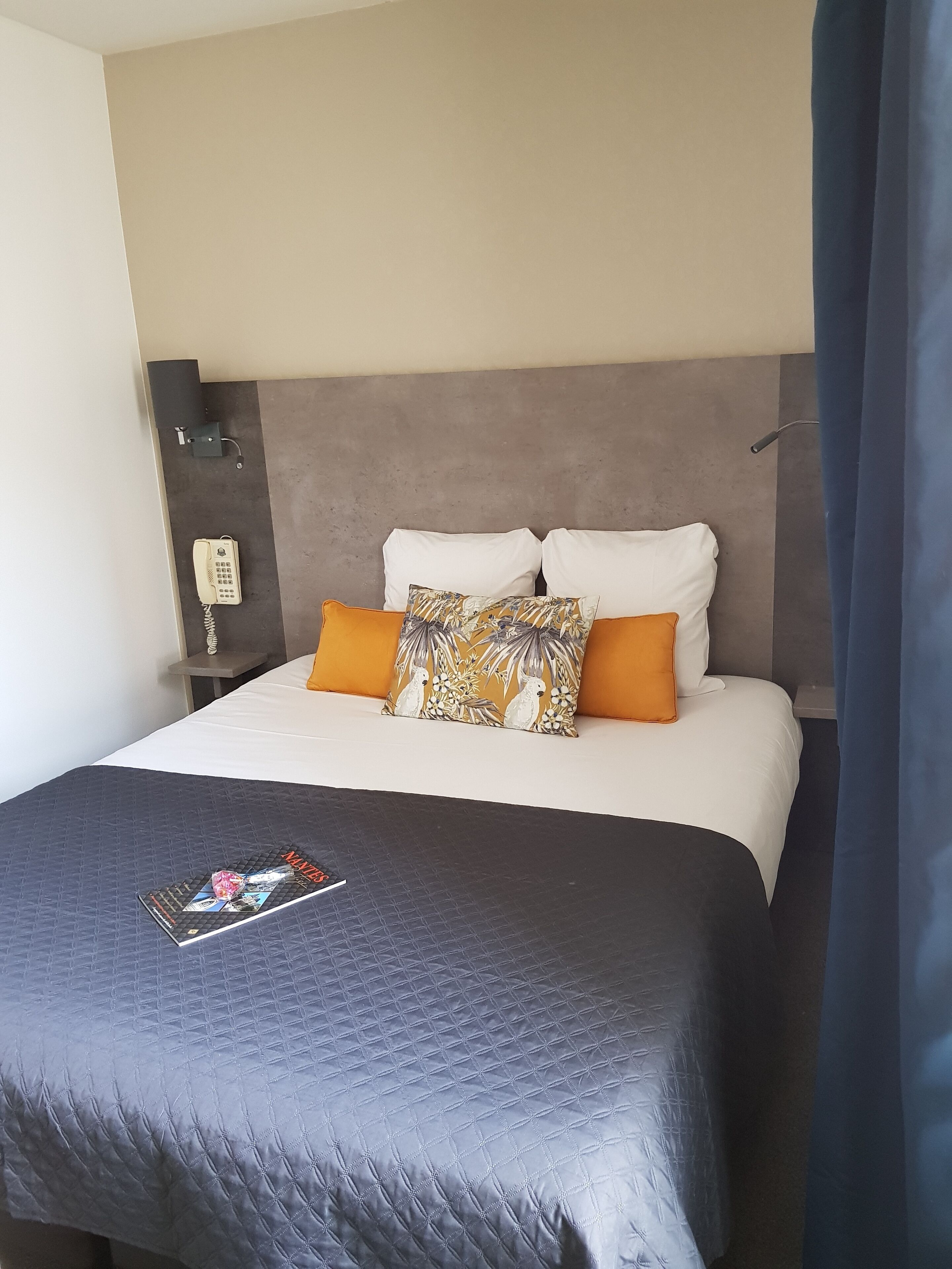 Un lit bien fait, avec une couverture matelassée, deux oreillers et un magazine posé sur le lit.