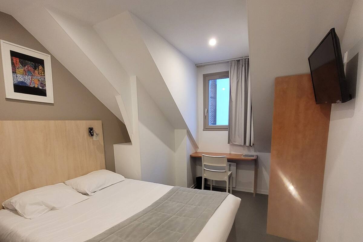 Ein Hotelzimmer mit Bett, Schreibtisch, Stuhl, Fernseher und einem Gemälde an der Wand.