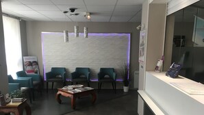 Un espace d’accueil au design moderne, comprenant un comptoir de réception, plusieurs coins salon avec des fauteuils, une table basse et un mur décoratif à motifs texturés.