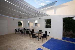 A covered outdoor dining area with tables and chairs, a white wall, and a blue carpet. - Balarte Hotel (Modica)