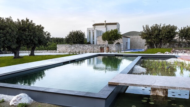 A modern outdoor pool area with stone walls and a building in the background. - Balarte Hotel (Modica)