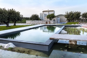 A modern outdoor pool area with stone walls and a building in the background. - Balarte Hotel (Modica)