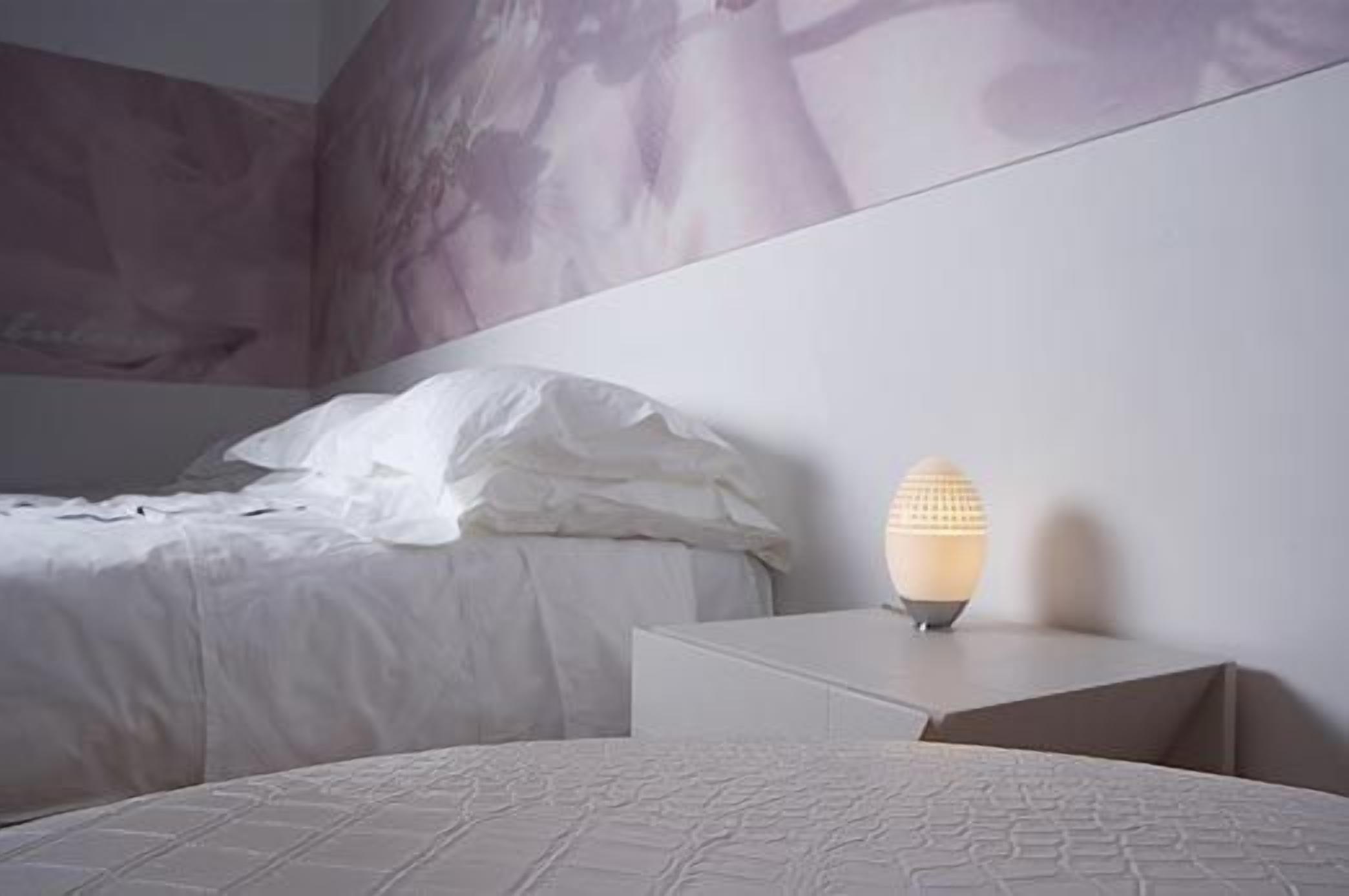 Un dormitorio moderno con cama, mesita de noche y lámpara de pared.