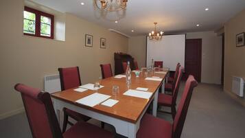 Une salle de conférence avec une longue table, des chaises rouges, un lustre et un tableau blanc.