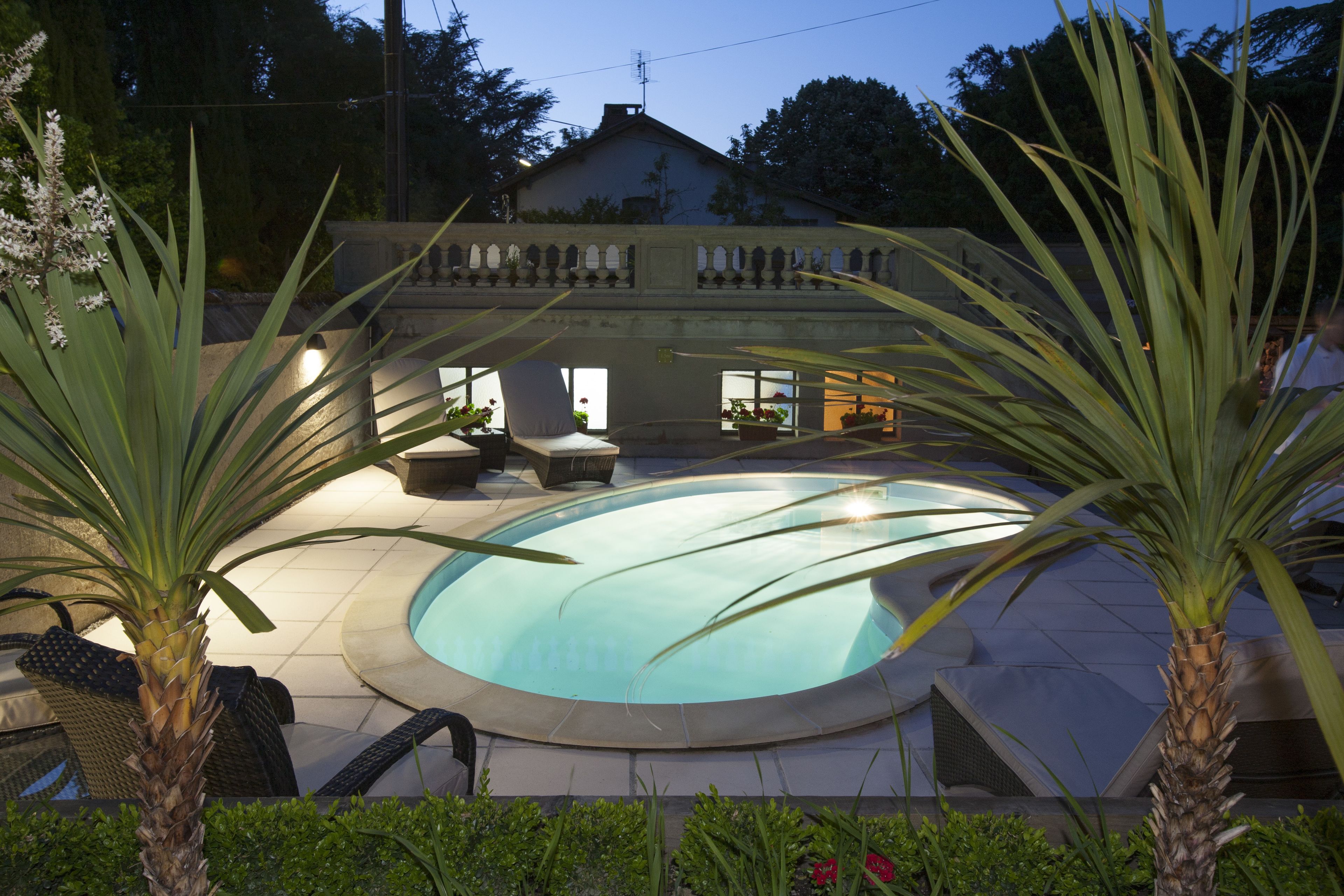 Ein Swimmingpool mit einer umlaufenden Terrassenanlage, inklusive Liegestühlen und einem kleinen Gebäude mit Fenstern.
