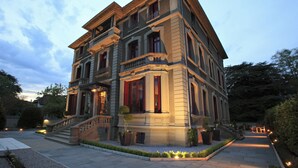 Un edificio grande de varios pisos con una entrada imponente, una escalera y un jardín bien cuidado.